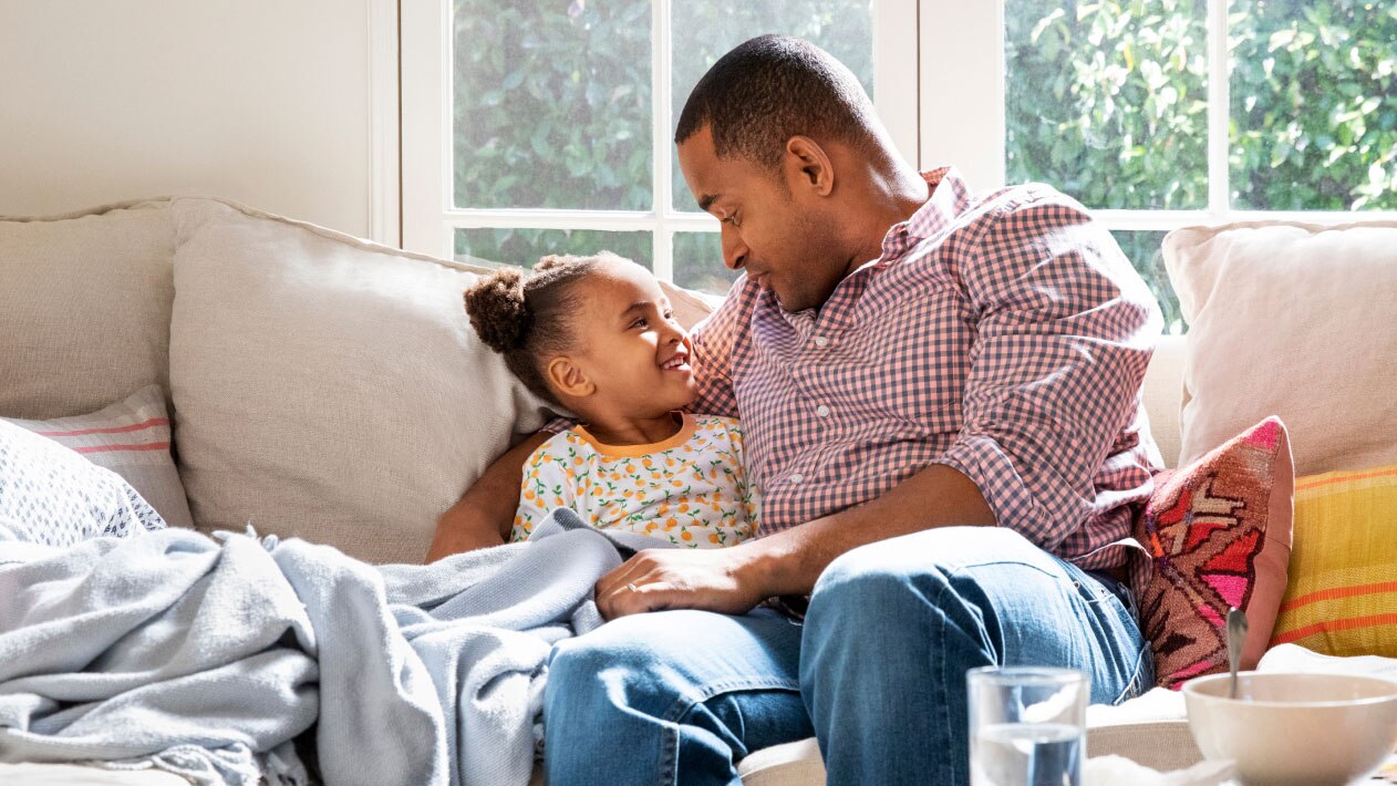 A father spends time with his daughter on their couch.