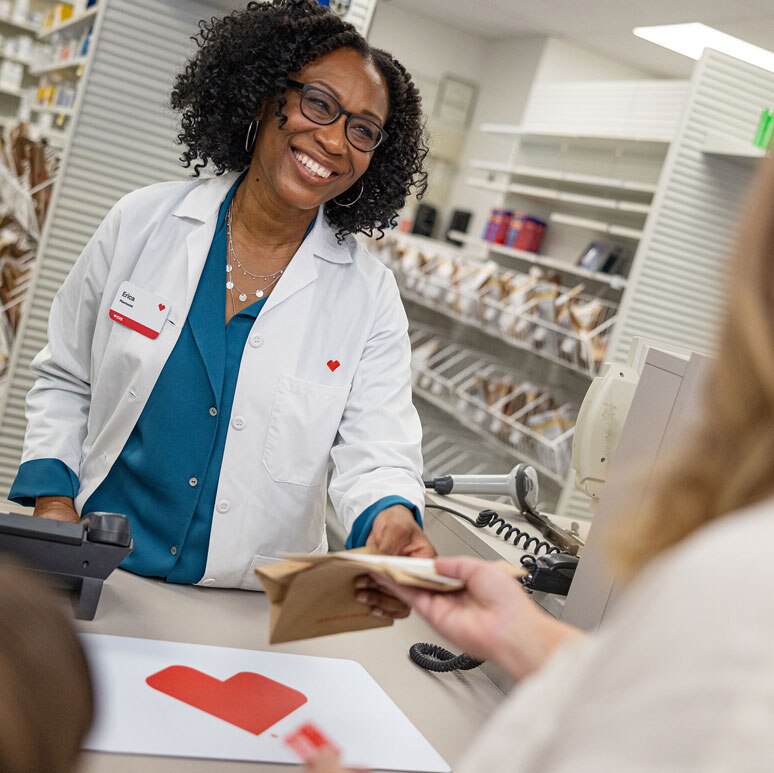 A CVS pharmacist hands a prescription package to a customer.